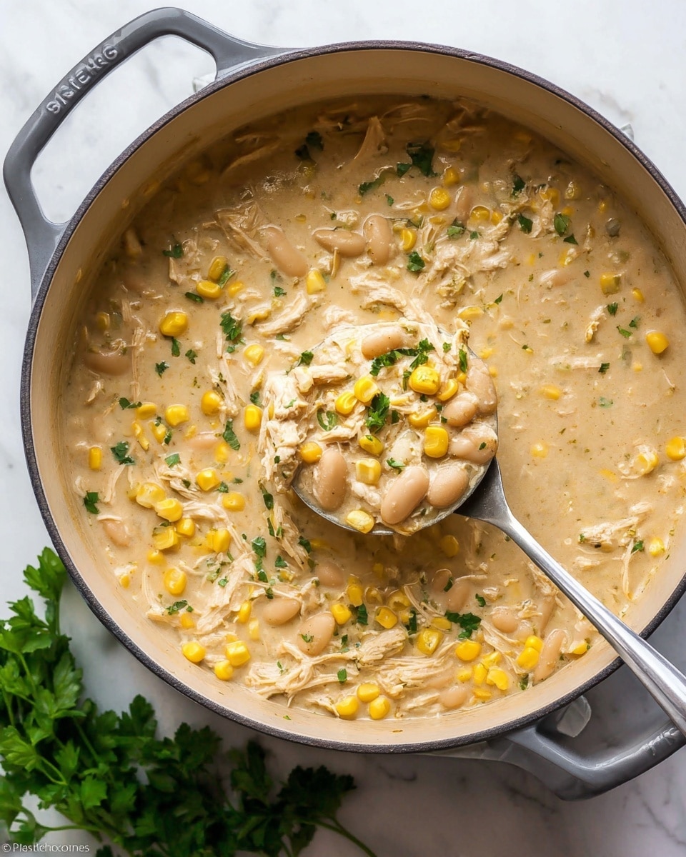 A large gray pot with a gray handle holds a creamy soup filled with three main layers visually: the soup base is light beige and smooth, filled with shredded white chicken strips and plump white beans; scattered bright yellow corn kernels add pops of color throughout the dish; small green herb pieces sprinkled on top create a fresh look. A silver ladle lifting some soup shows the thick, hearty texture clearly. Around the pot, fresh green parsley adds color against the white marbled surface below. photo taken with an iphone --ar 4:5 --v 7