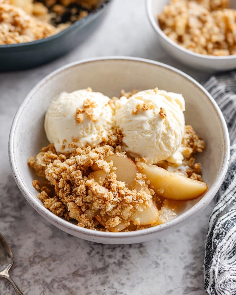 A white bowl filled with apple crumble dessert showing three main layers: the bottom layer has tender, soft apple slices in a pale beige color, the middle layer is made of golden brown crumbly oat topping with a crisp texture, and on top there are two small scoops of creamy white vanilla ice cream sprinkled with bits of the crumble. The bowl is set on a white marbled texture with parts of two more bowls and a striped cloth visible nearby. Photo taken with an iphone --ar 4:5 --v 7