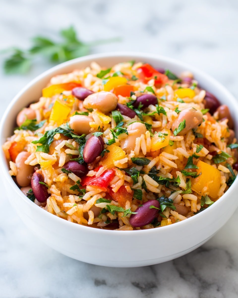 A white bowl filled with a colorful mixture of cooked rice, beans, chopped red and yellow bell peppers, and fresh green herbs scattered on top. The rice is soft and fluffy with an orange tint, evenly mixed with whole light brown beans. Bright red diced tomatoes and finely chopped dark green leafy vegetables add contrast and freshness throughout the dish. The bowl is placed on a white marbled surface, enhancing the vibrant colors of the food. photo taken with an iphone --ar 4:5 --v 7
