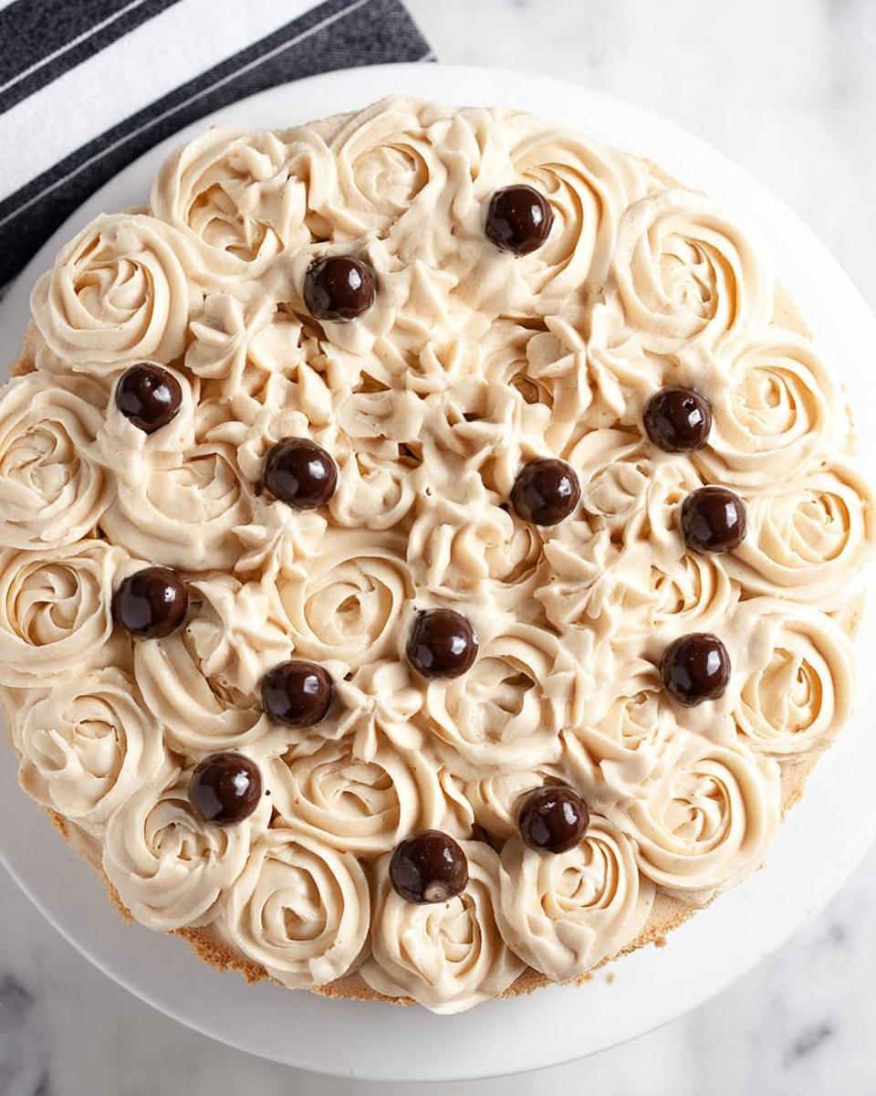 A round pie topped with many piped swirls of light beige cream, each swirl smooth and detailed with a soft texture, covering almost the whole pie surface densely. Small, shiny, dark brown round chocolate balls are placed evenly on top, adding contrast with their smooth and glossy appearance. The pie crust is visible slightly at the edges under the cream. The pie is set on a white plate on a white marbled surface with a black and white striped cloth partially visible at the top side. photo taken with an iphone --ar 4:5 --v 7