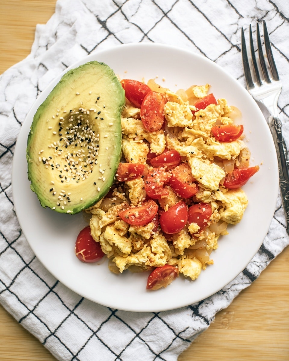 A white plate sits on a white marbled surface, holding a dish made of scrambled eggs mixed with soft cooked onion pieces that are pale yellow, and chunks of red cherry tomatoes scattered throughout. To the side of the eggs is half an avocado with bright green flesh sprinkled generously with black and white sesame seeds. The plate is neatly set with a fork resting on a white cloth with a black grid pattern above it. Photo taken with an iphone --ar 4:5 --v 7