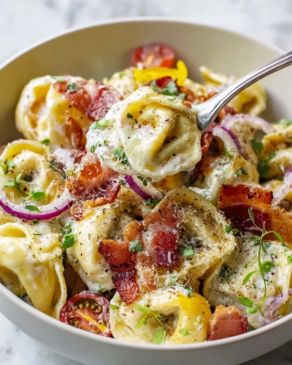 The image shows a close-up of a white bowl filled with several layers of tortellini pasta coated in a creamy white sauce. On top of the pasta are crispy pieces of reddish-brown bacon scattered throughout, finely grated cheese, and a sprinkle of black pepper. Thin slices of purple onion and small green herbs add color contrast, with a few yellow and red tomato slices visible near the edges. A silver fork lifts one tortellini piece covered in sauce and bacon. All of this rests on a white marbled surface. photo taken with an iphone --ar 4:5 --v 7