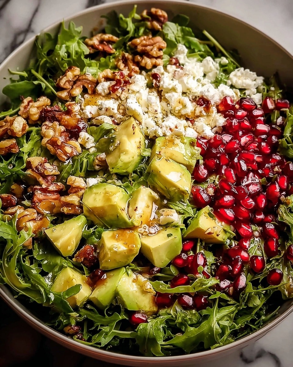 A large bowl filled with a fresh salad showing three main layers: the bottom layer is dark green leafy arugula with a slightly rough texture, the middle layer features evenly spread chunks of light green avocado and small, juicy, bright red pomegranate seeds, and the top layer is a sprinkling of crumbled white cheese and chopped golden brown walnuts. The salad is drizzled with a shiny, slightly thick dressing giving it a light glossy look. The bowl sits on a white marbled surface. photo taken with an iphone --ar 4:5 --v 7