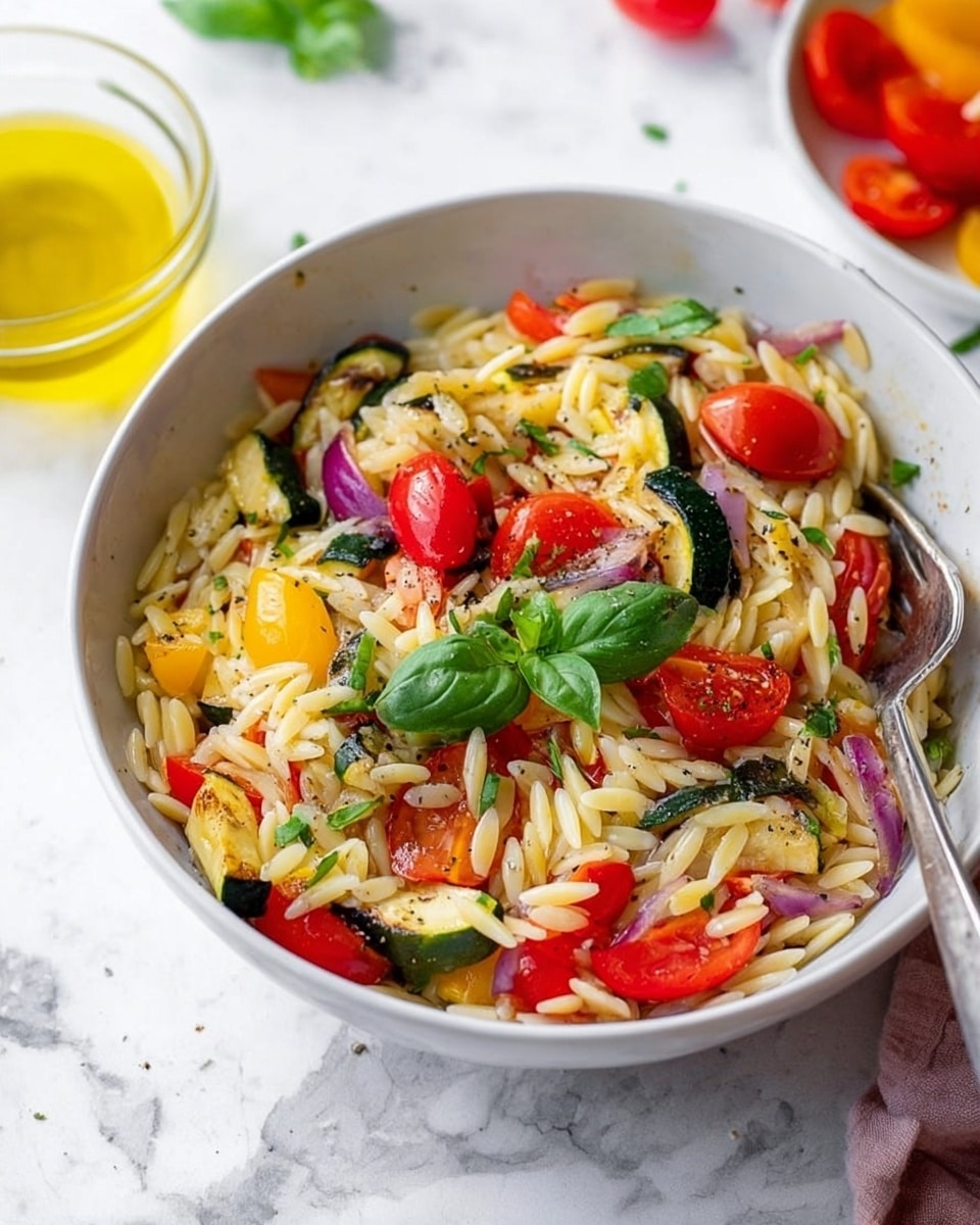 The image shows a white bowl filled with orzo pasta mixed with colorful vegetables. The pasta is a light yellow color and forms the base layer. Scattered throughout are bright red cherry tomato halves, small pieces of grilled zucchini with green and slightly charred yellow skin, and chunks of purple onion. A few fresh green basil leaves sit on top for garnish. The dish is lightly sprinkled with black pepper. The bowl rests on a white marbled surface, with a metal fork placed inside the bowl on the right side. In the background, there are some sliced cherry tomatoes and a small glass bowl of yellow olive oil visible. Photo taken with an iphone --ar 4:5 --v 7