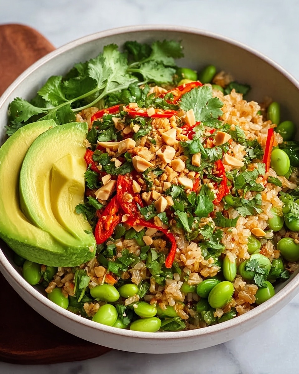 A bowl filled with a colorful rice dish sits on a white marbled surface. The base layer is light brown cooked rice mixed with bright green edamame beans and small pieces of green vegetables. On top, there are thin slices of red pepper and several fresh green cilantro leaves, sprinkled with crushed peanuts. On one side of the bowl, smooth avocado slices lean against the rice, adding a creamy yellow-green color and soft texture. The bowl itself is white, slightly deep with a clean round shape. Photo taken with an iphone --ar 4:5 --v 7