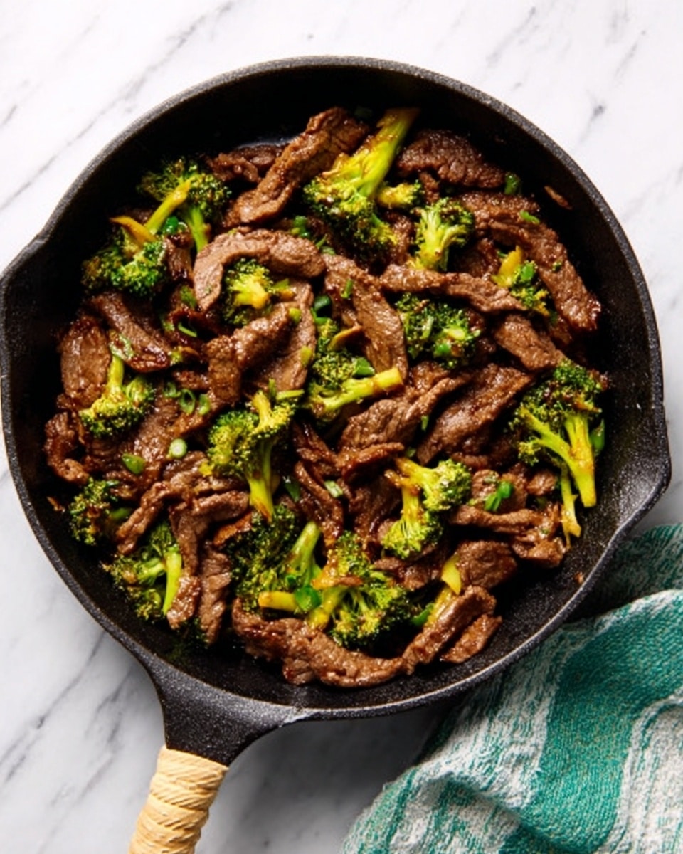 The image shows a black cast iron pan filled with cooked beef strips and small broccoli florets. The beef is browned and slightly glossy, mixed evenly with the green broccoli pieces that add a pop of color. The dish looks well-cooked with a slightly oily texture, and the pan has a rustic feel with a light-colored tan handle. The pan rests on a white marbled surface with a green and white cloth partially visible on the right side. Photo taken with an iphone --ar 4:5 --v 7