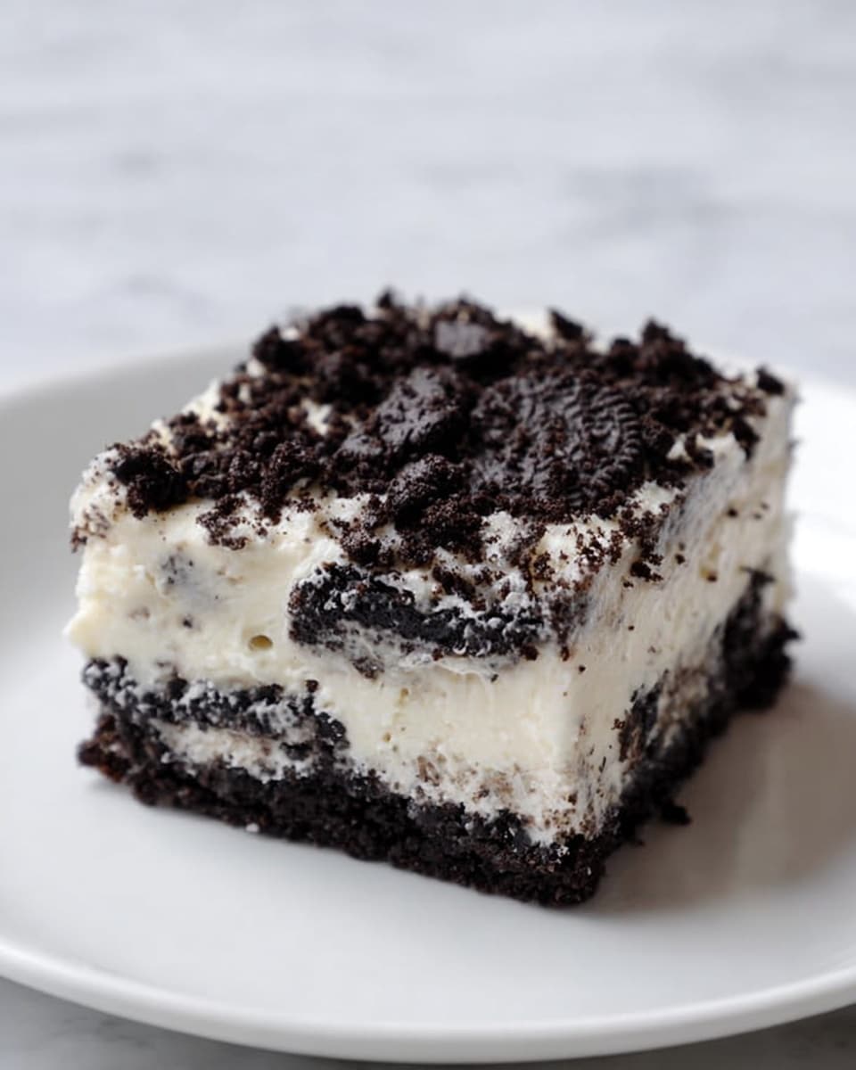 The image shows a white bowl containing a layered dessert with four visible layers. The bottom layer is dark brown and crumbly, likely crushed cookies. Above it is a smooth caramel layer with a rich golden-brown color. The third layer is thick and creamy white, topped with crushed dark cookie crumbs sprinkled evenly on the surface. A silver spoon is scooping some of the dessert, revealing the layers clearly. In the background, there is another bowl with a similar dessert and a white marbled texture surface beneath everything. Photo taken with an iphone --ar 4:5 --v 7
