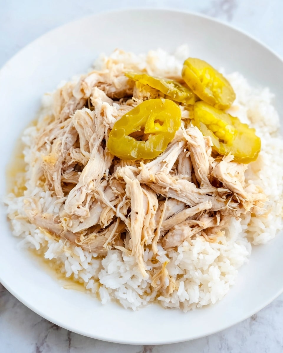 A white plate holds a bed of soft white rice as the base layer, topped with a generous layer of light brown shredded chicken that looks tender and moist. Three pale yellow pickled peppers are scattered on top of the chicken, adding a pop of color and texture contrast. The plate is set on a white marbled surface, giving a clean and simple background. The photo taken with an iphone --ar 4:5 --v 7