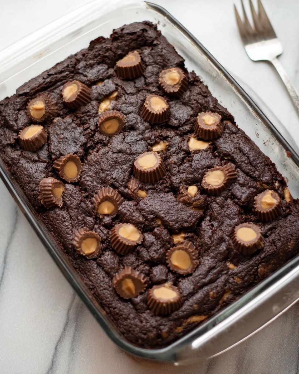 A rectangular glass dish filled with dark chocolate batter as the base layer, topped unevenly with light tan spoonfuls of peanut butter dough scattered across the surface. Small dark brown mini chocolate chips and mini peanut butter cups are sprinkled generously over both layers, creating a textured and rich look. The dish sits on a white marbled surface with packages of Triple Chocolate Fudge cake mix, Reese's minis, and Nestle Toll House semi-sweet chocolate chip cookies in the blurred background. photo taken with an iphone --ar 4:5 --v 7