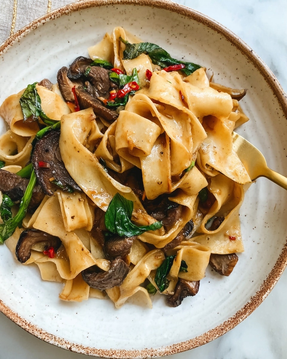 The dish shows a close-up view of wide, flat noodles that are light golden brown and slightly curled, mixed with dark brown mushroom slices that have a glossy texture, and pieces of cooked beef that are brown and tender-looking. Scattered throughout are green leafy herbs adding a fresh touch and small red chili flakes providing a hint of spice. The food is plated on a white speckled plate with a thin brown rim, and a golden fork slightly lifts a few noodles on the right side. The plate sits on a white marbled surface visible at the bottom left corner. Photo taken with an iphone --ar 4:5 --v 7