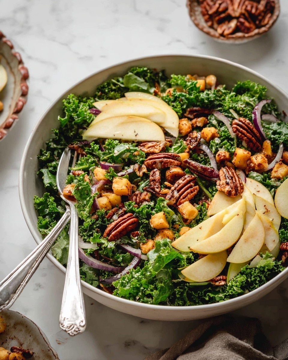 A large white bowl filled with a fresh salad showing a mix of three layers: the bottom layer has bright green curly kale leaves with a rough texture, the middle layer has thin slices of light yellow apple and purple-red onion rings scattered throughout, and the top layer features small, golden-brown roasted cubes, light golden chickpeas, and dark brown pecan nuts sprinkled on top. Two silver forks rest inside the bowl on the left side, and in the blurred background on a white marbled surface, there is a small white bowl with pecans in a brown fluted dish. photo taken with an iphone --ar 4:5 --v 7
